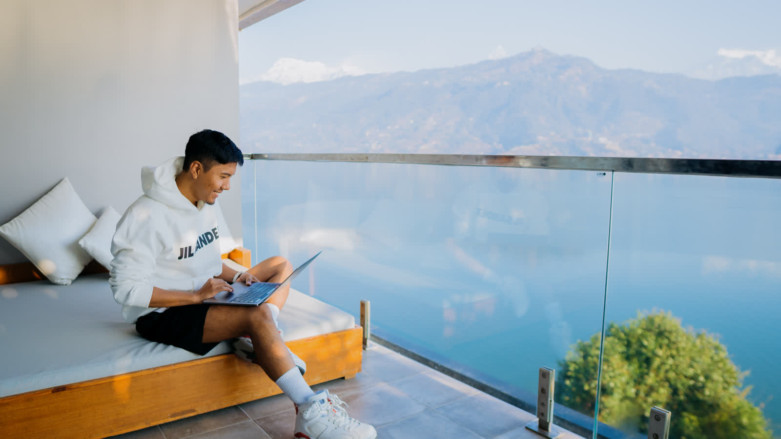 Nishang working on a laptop on a balcony overlooking the hills in Nepal